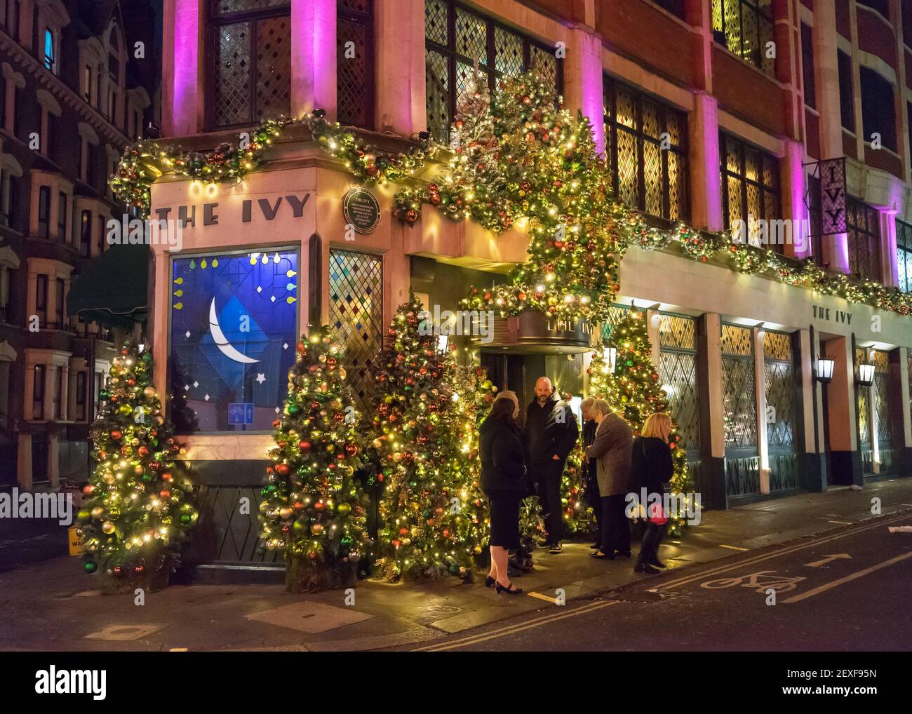 The Ivy Restaurant in London at night with stained glass windows and Christmas Lights and customers waiting to go inside. Stock Photo