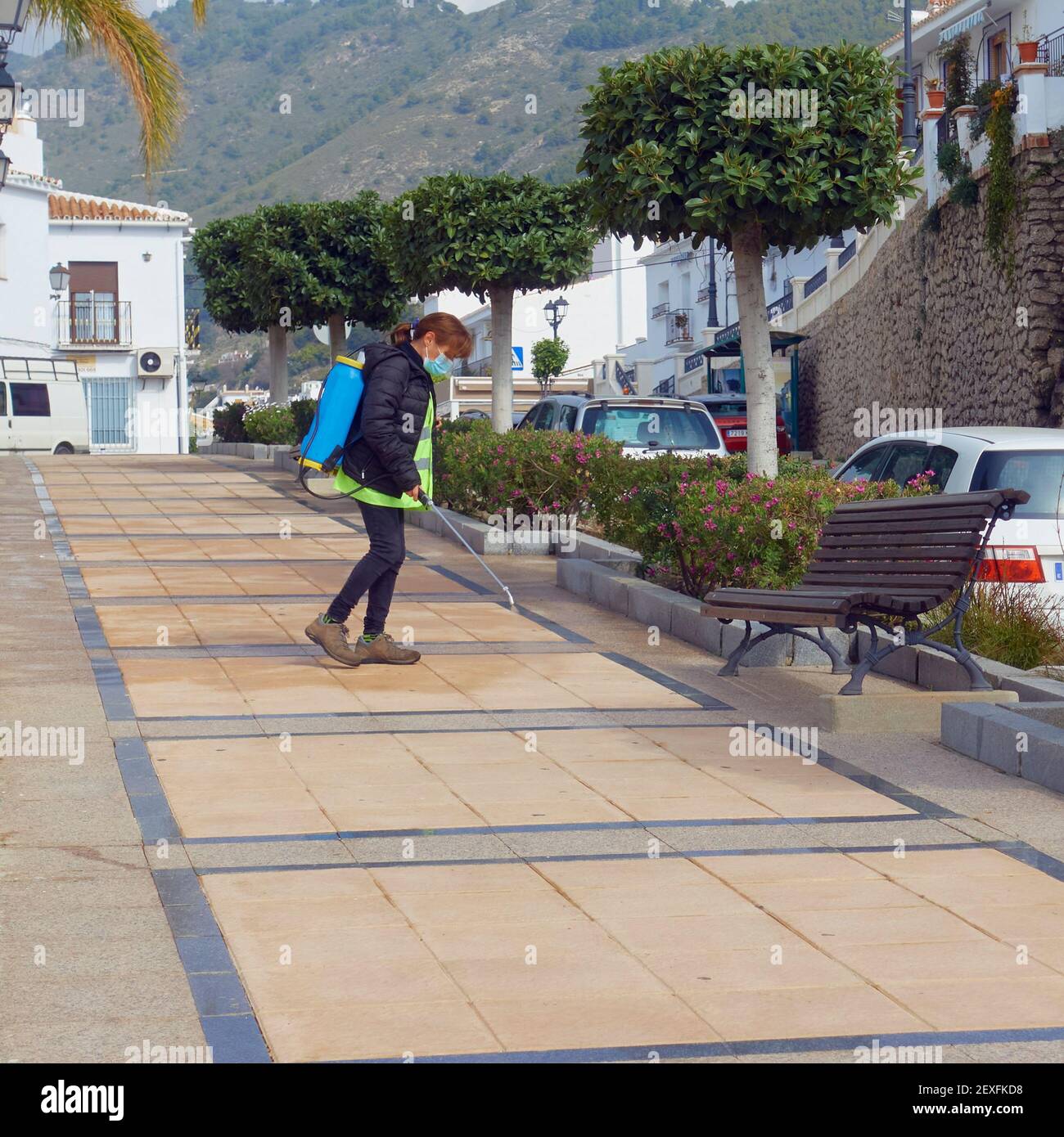 A female worker sprays disinfectant on the pavement to fight Covid-19 in the whitewashed tourist village of Frigiliana, Malaga, Spain Stock Photo