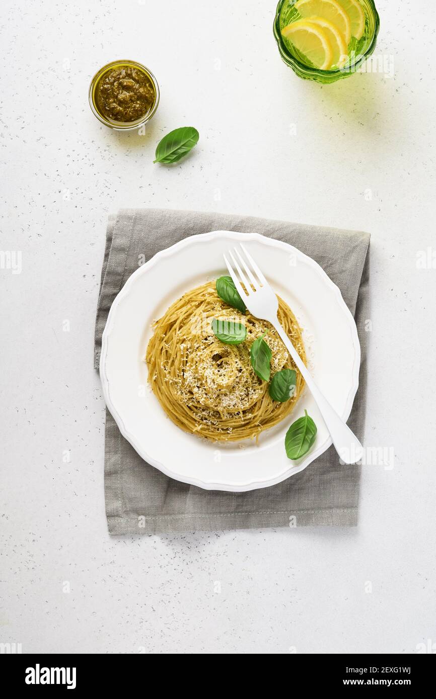 Pasta spaghetti with pesto sauce and fresh basil leaves in white bowl. Grey background. Mock up. Top view. Stock Photo