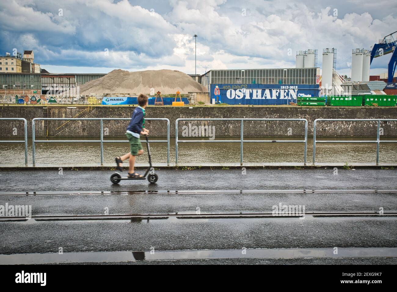 Boy riding his scooter passing East harbor, Frankfurt, Germany Stock Photo