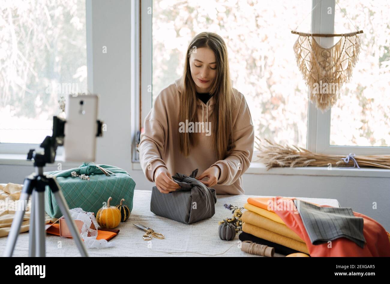 Woman wraps Furoshiki gift in zero waste style and record vlog, master class on cell phone. Furoshiki Japanese Gift Wrapping. Zero waste, eco-friendly Stock Photo