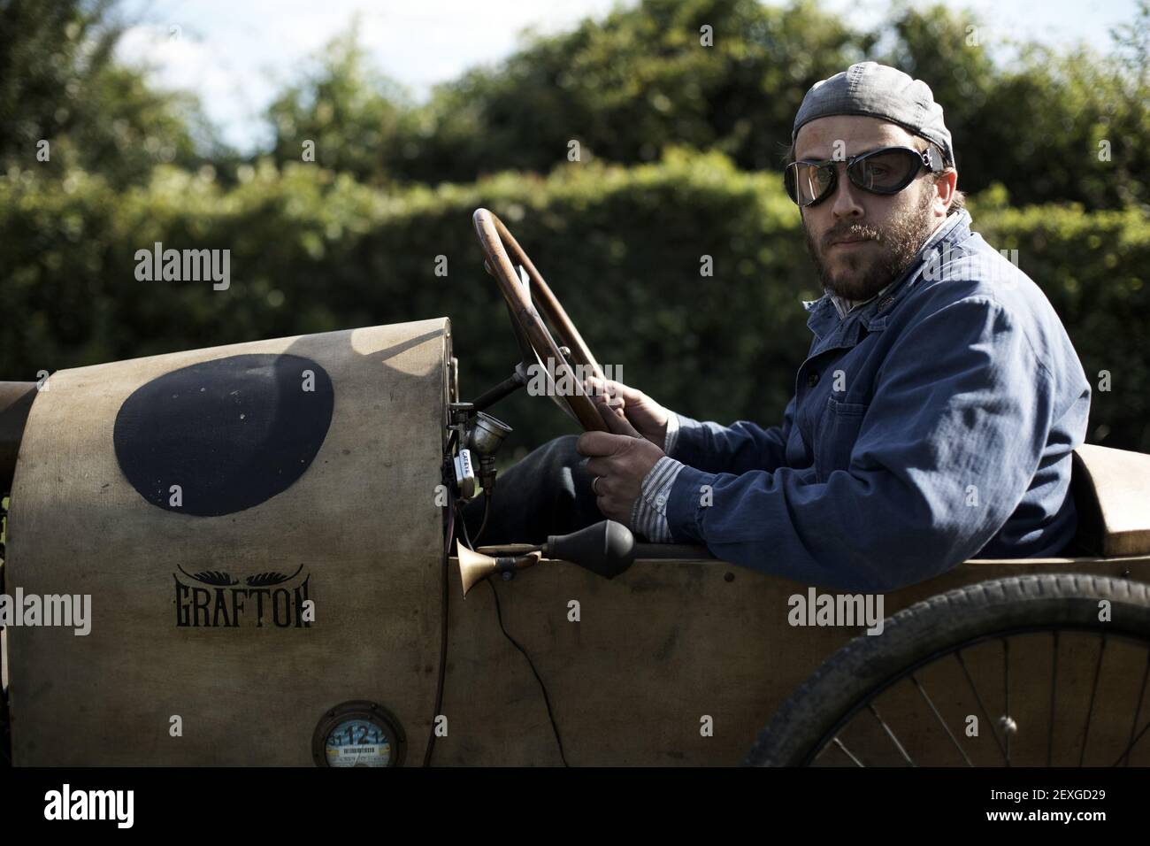 https://c8.alamy.com/comp/2EXGD29/road-trip-with-a-vintage-grafton-cycle-car-man-with-hat-and-goggles-vintage-look-driving-on-a-road-2EXGD29.jpg