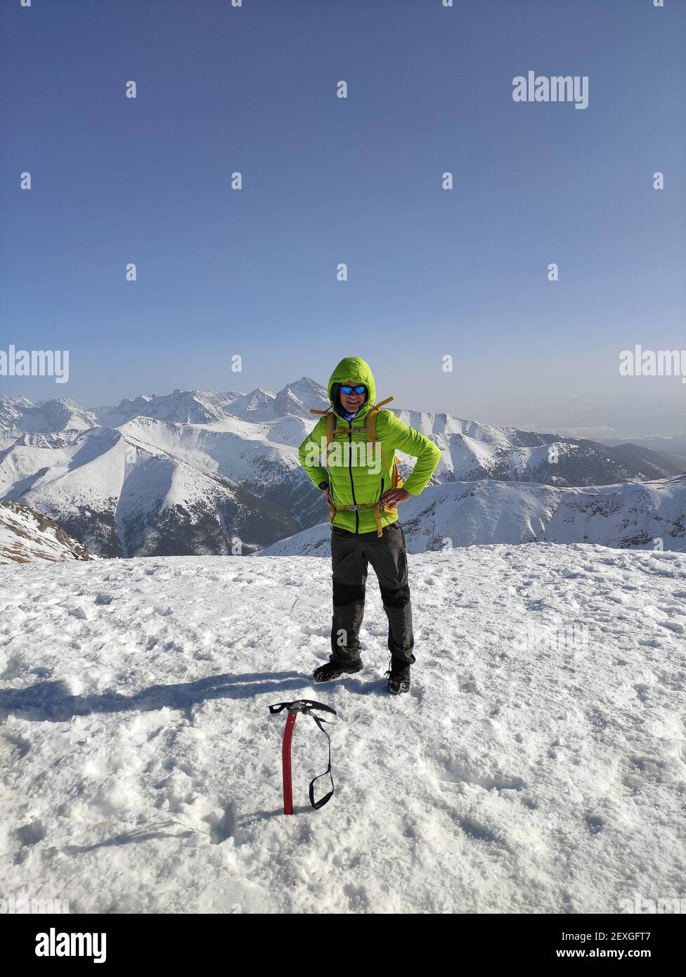 Happy mountaineer reaches the top of a snowy mountain in a sunny winter. Stock Photo