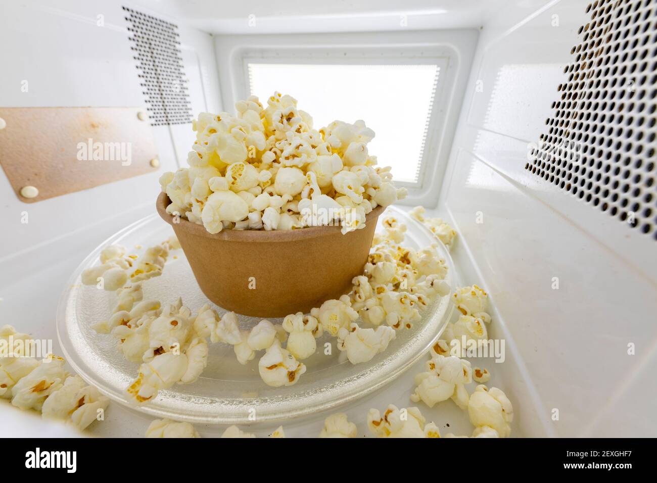 Spilled popcorn in the microwave. Salty snack prepared in the kitchen appliance. Light background. Stock Photo