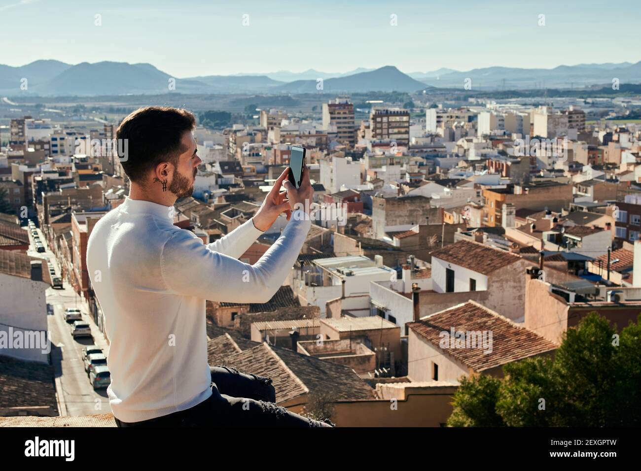Man is sitting on a rooftop taking pictures with his phone Stock Photo