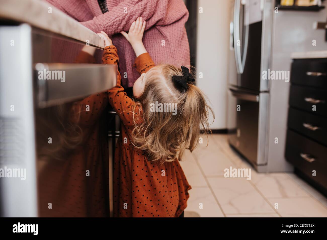 Toddler girl reaches for her mom in the family kitchen Stock Photo