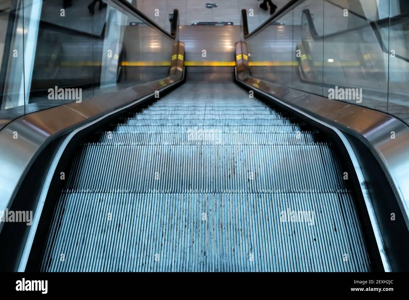 Shot of an escalator moving downwards, glass handrails, metal steps