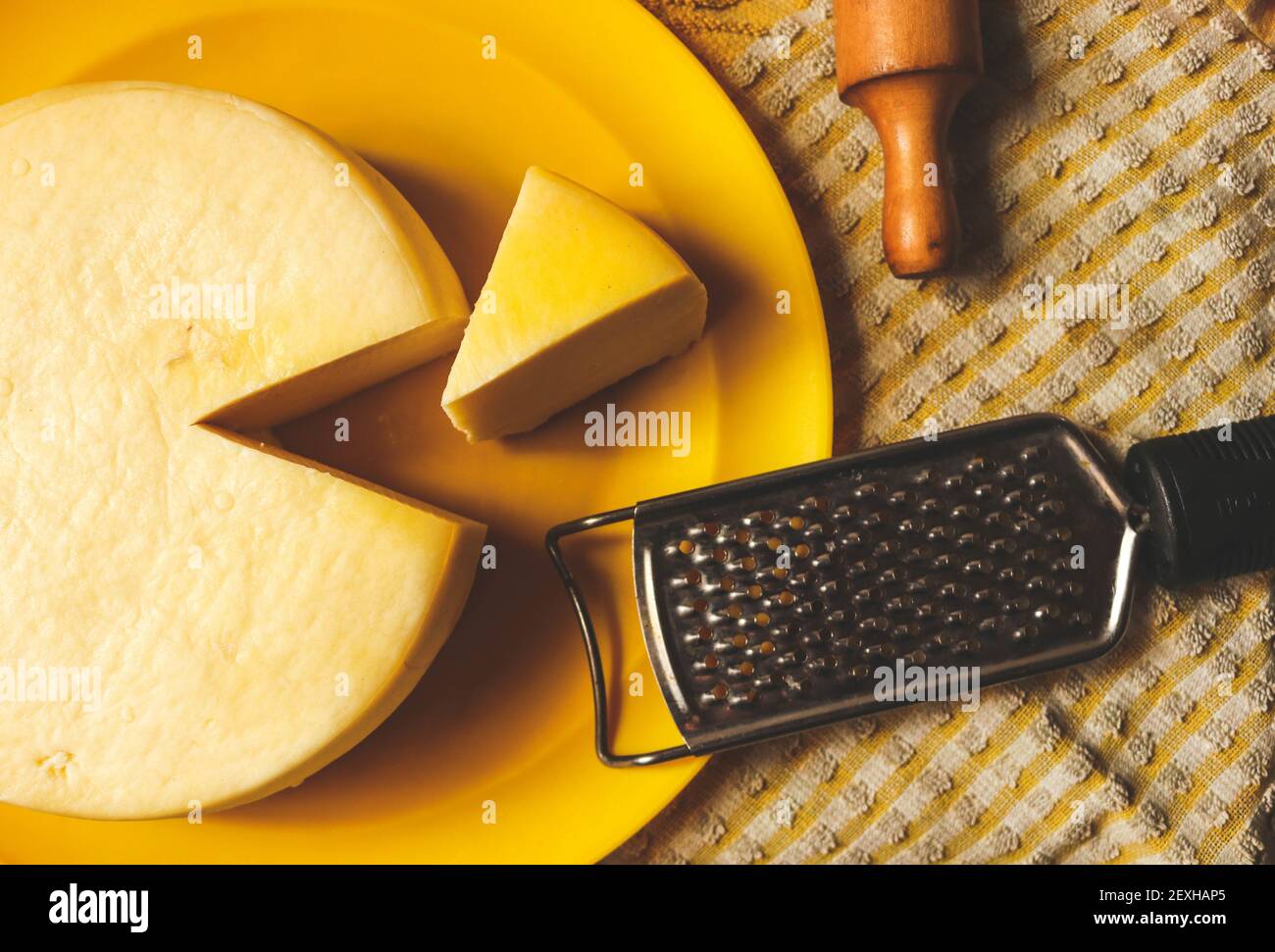 A top view of a cut gouda cheese on a plate on the table with a rolling