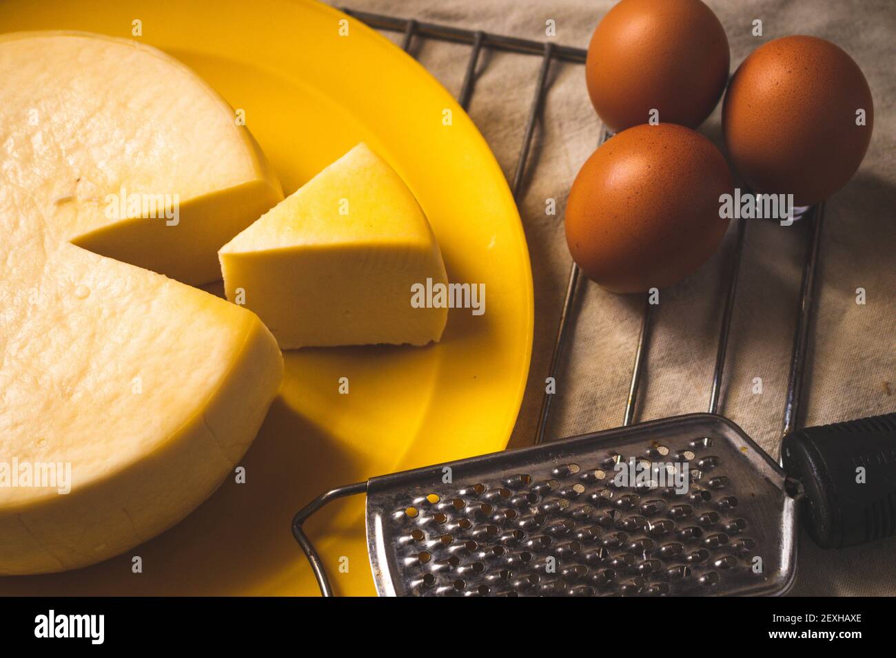 A closeup of a cut gouda cheese on a plate on the table with eggs and a