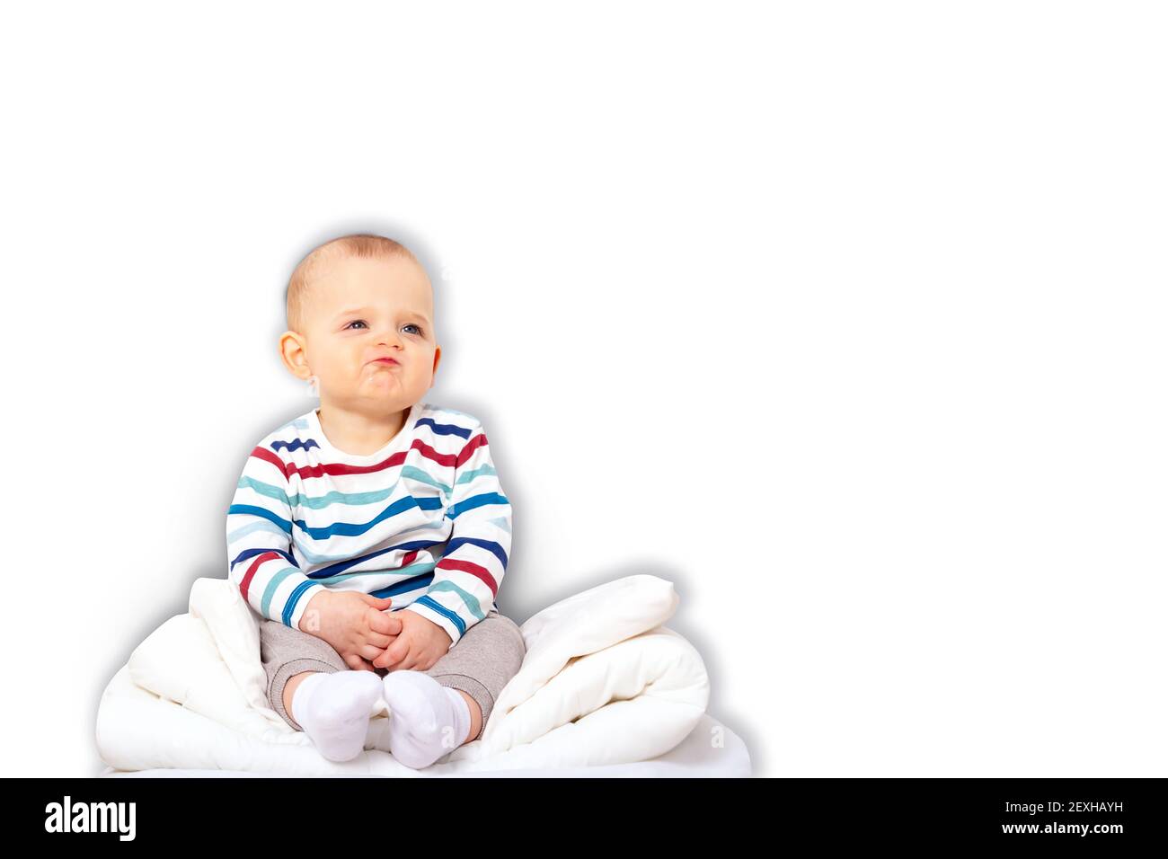 Funny caucasian baby boy in striped t-shirt sitting on pillow mountain. Isolated on white background.  Stock Photo