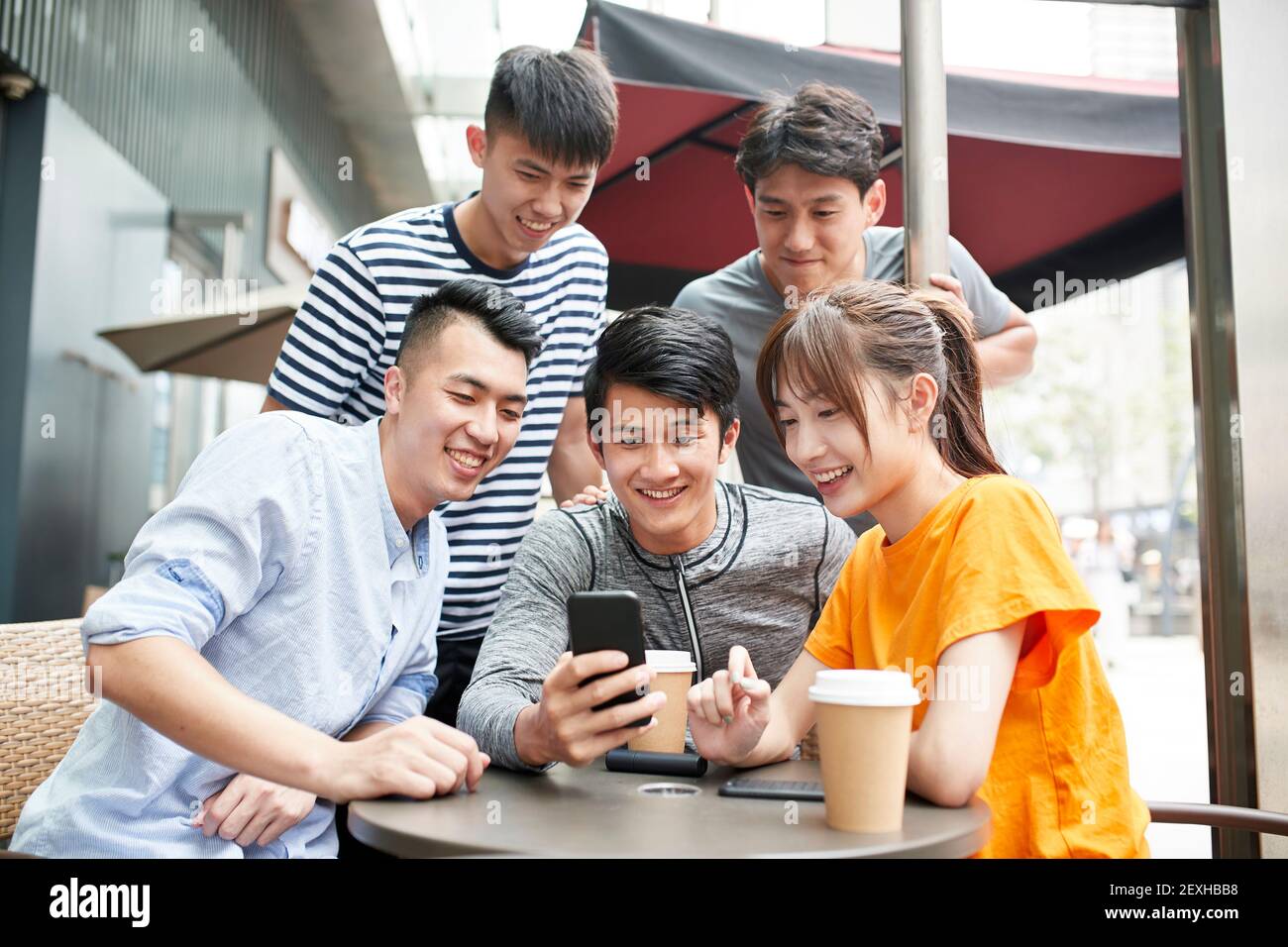 group of young asian adults four men and and a woman looking at mobile phone together outdoors Stock Photo