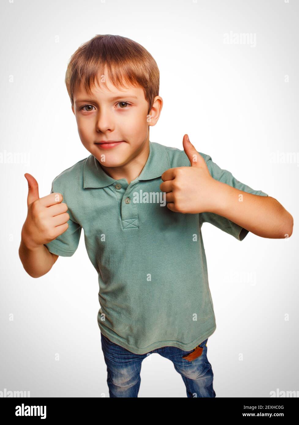 Blonde boy kid in blue shirt holding thumbs up, showing the sign Stock Photo