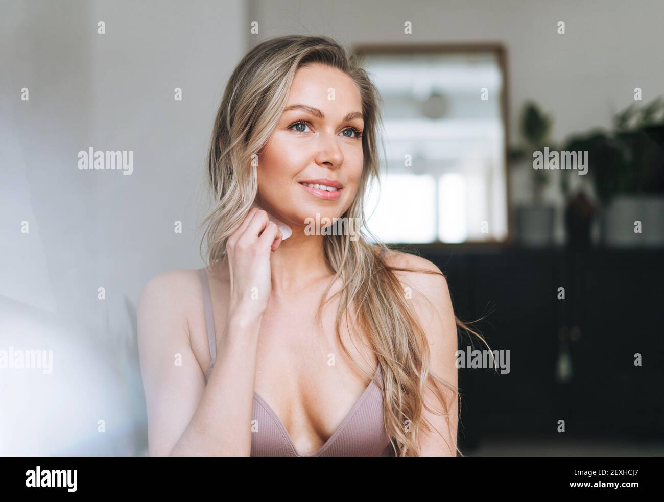 Blonde smiling woman 35 year plus clean fresh face and hands with long hair does facial massage with gouache scraper in underwear Stock Photo