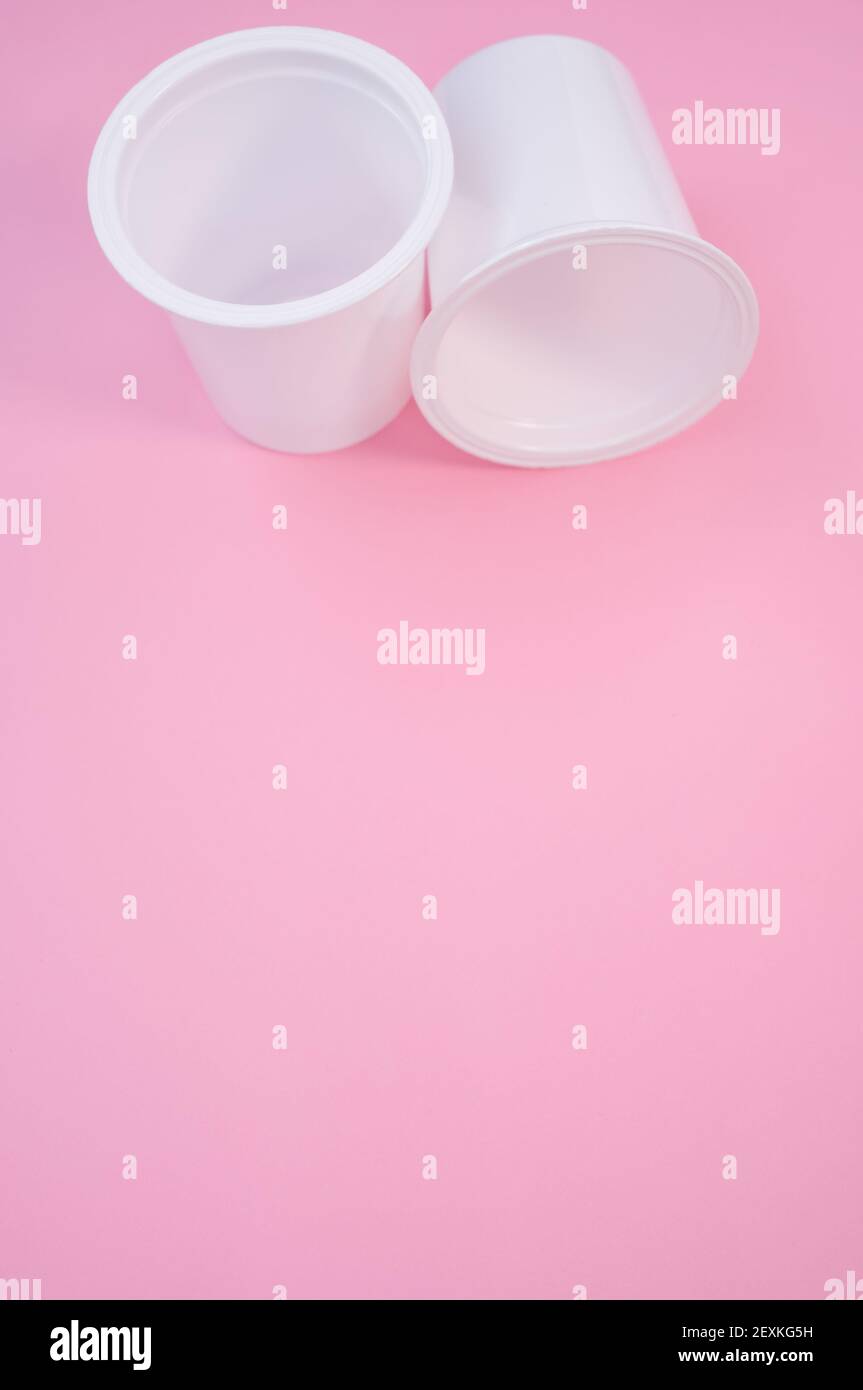 A vertical shot of plastic white cups on a pastel pink surface for a ...