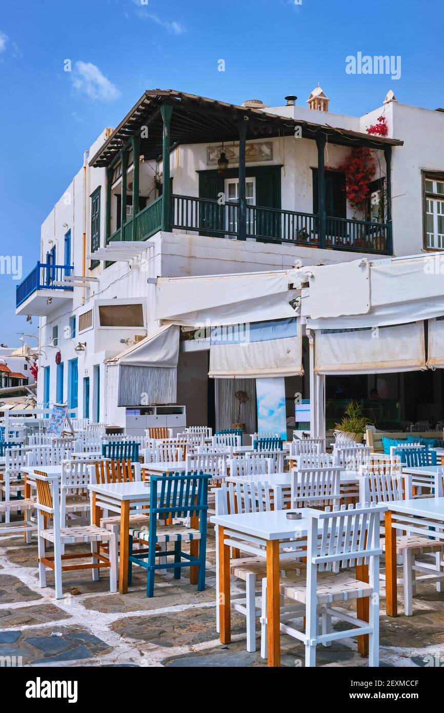 Outdoor cafe or restaurant in typical Greek island town. Church, blue dome, tourists roam. Sunny summer day, Mykonos, Cyclades, Greece. Vertical shot Stock Photo