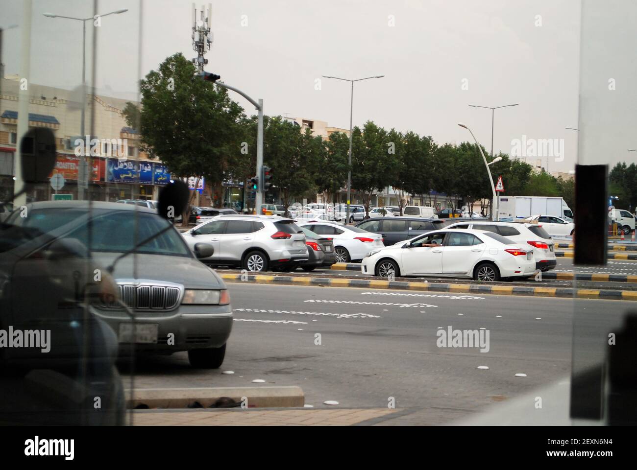 RIYADH, SAUDI ARABIA - Feb 18, 2021: traffic on road waiting for signal,trees and shops behind,beautiful cloudy weather Stock Photo