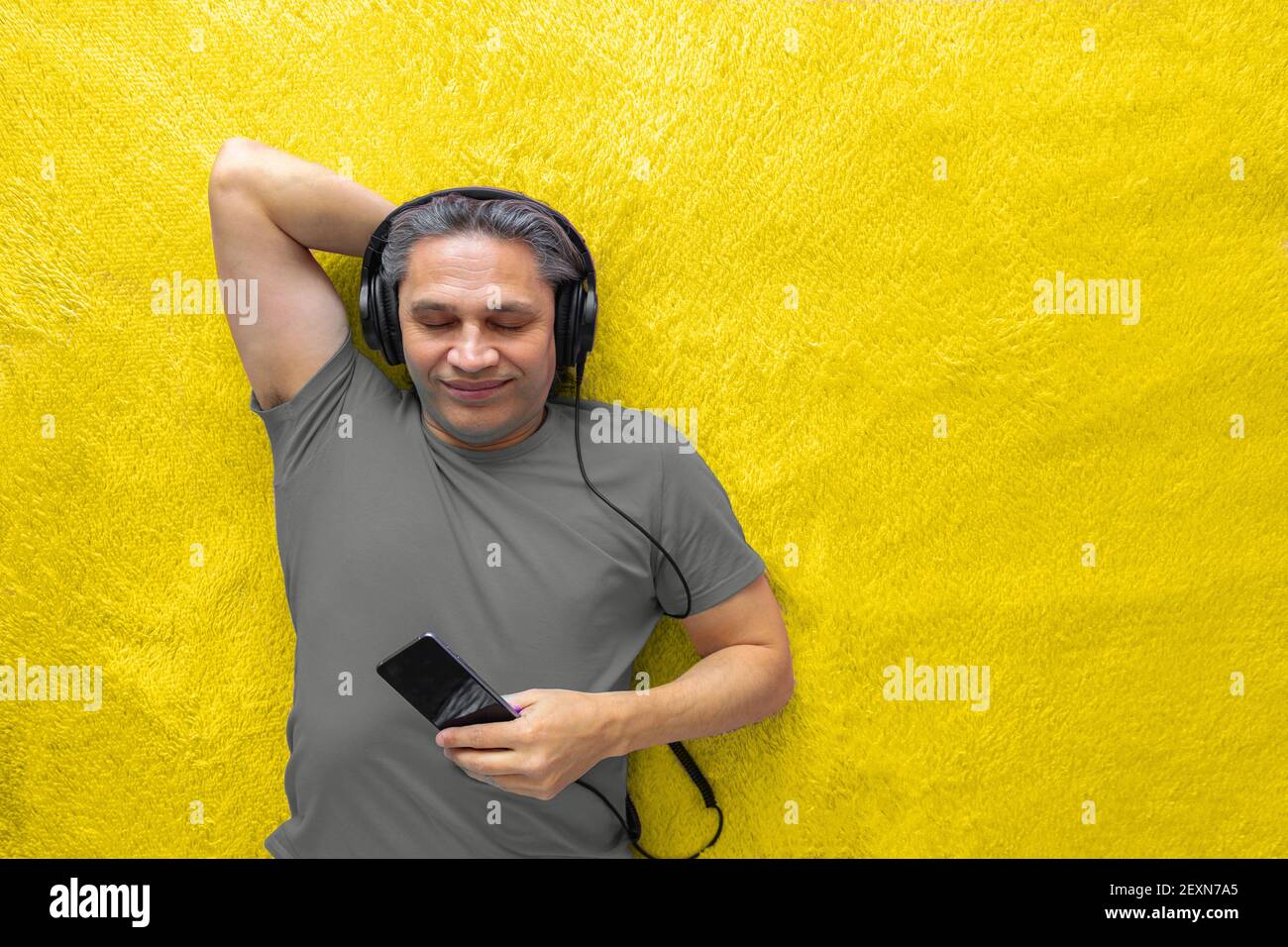 50-year-old man listens to music with headphones at home, lying on the bed. Relaxing, enjoying. Stock Photo