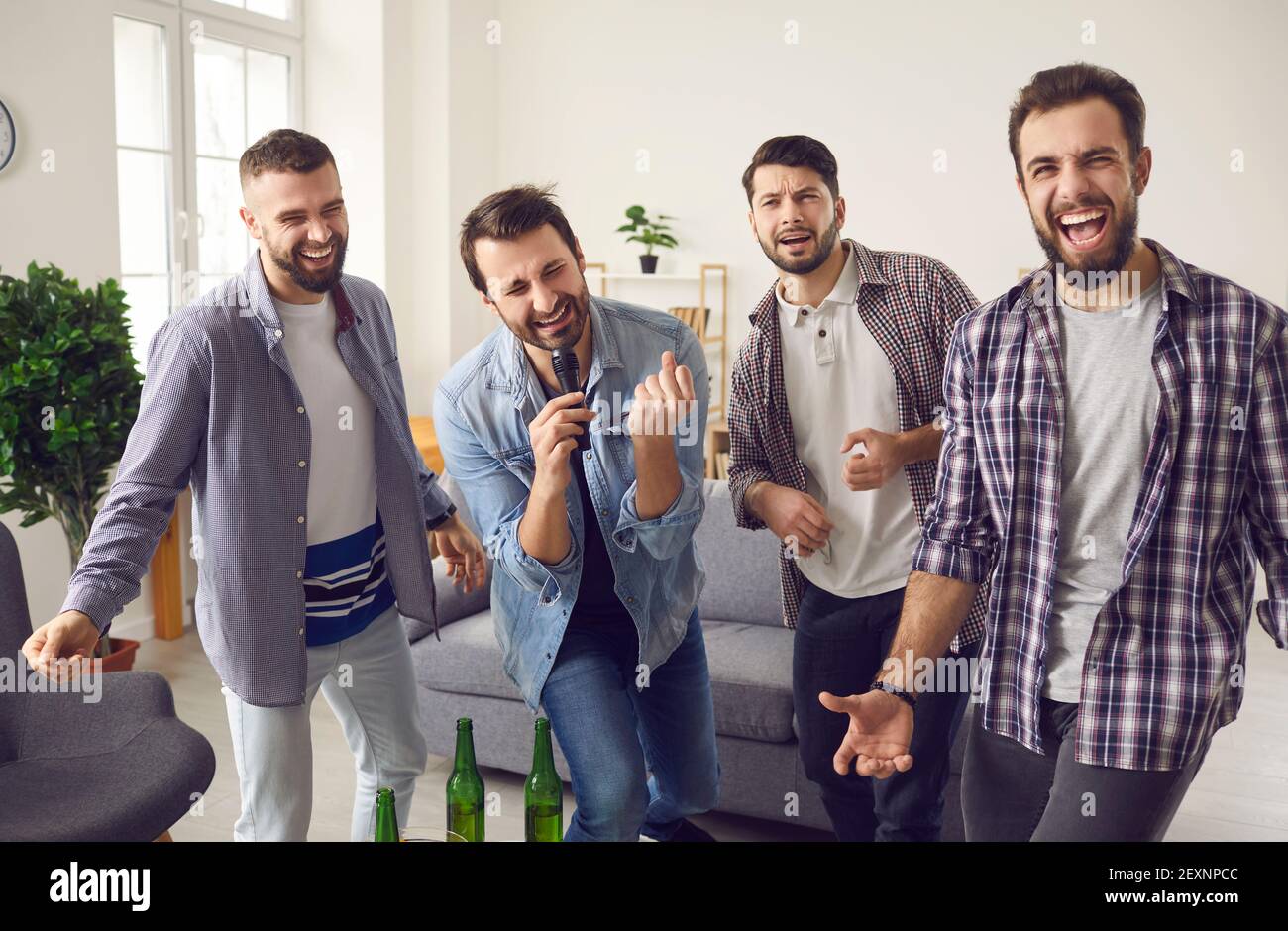 Cheerful young men friends having home party with bear and snacks and singing karaoke Stock Photo