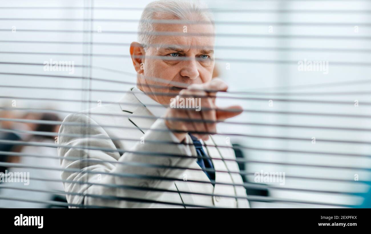 smiling Mature businessman looking through office window blinds. Stock Photo