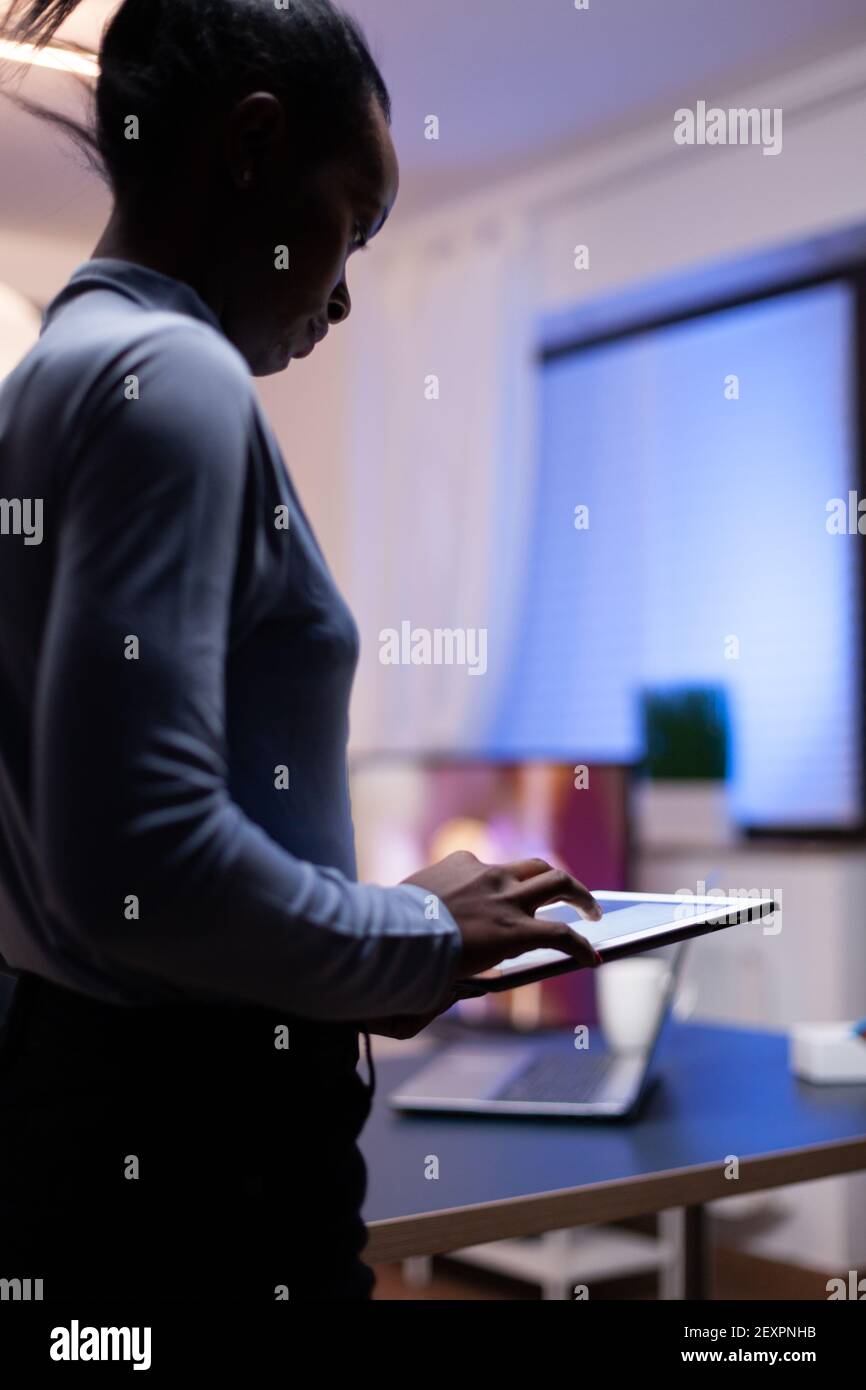 Dark skinned woman utilises tablet pc in home office late at night ...