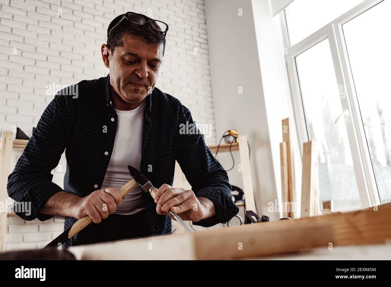Middle-aged man carpenter working in a workshop with chisel and hammer Stock Photo