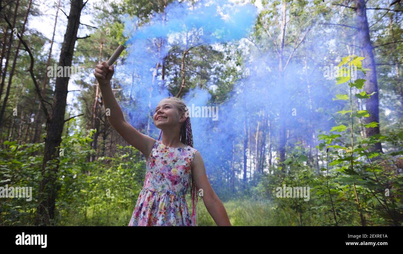 A teenage girl with blue smoke walks in the forest. Stock Photo