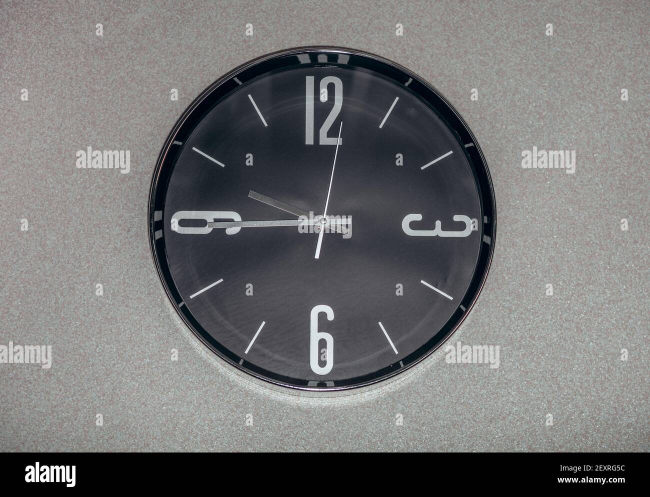 Black wall clock with a second hand hanging on the wall. A minimalist