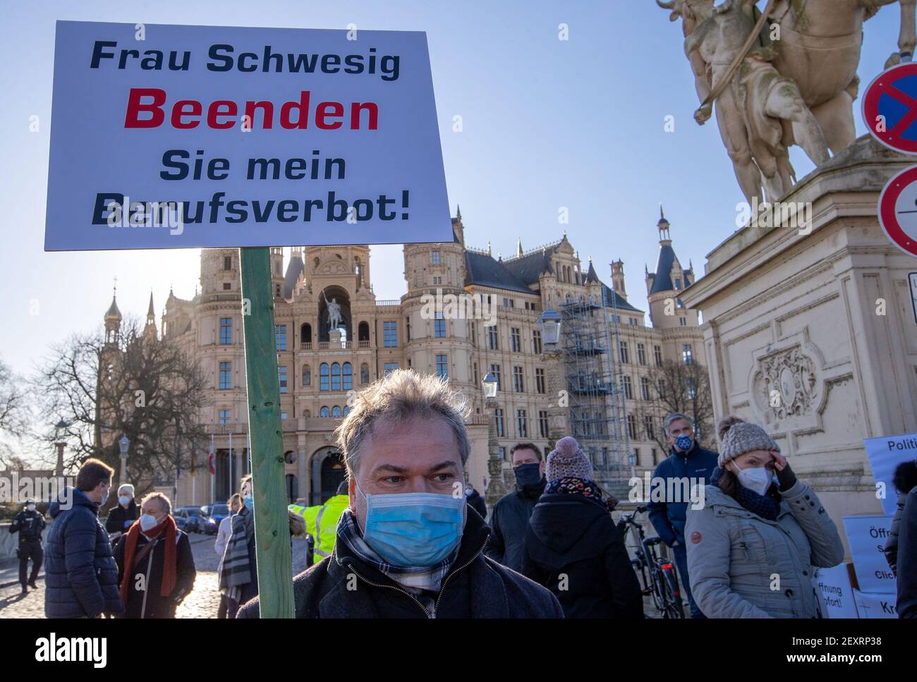 Schwerin, Germany. 05th Mar, 2021. Traders, restaurateurs and fitness studio operators protest against the ongoing Corona closures in front of the state parliament building in Schwerin Castle, one participant holds a sign 'Frau Schwesig Beenden Sie mein Berufsverbot!'. The state parliament meets for a special session to discuss further Corona protection measures for Mecklenburg-Vorpommern. Credit: Jens Büttner/dpa-Zentralbild/dpa/Alamy Live News Stock Photo