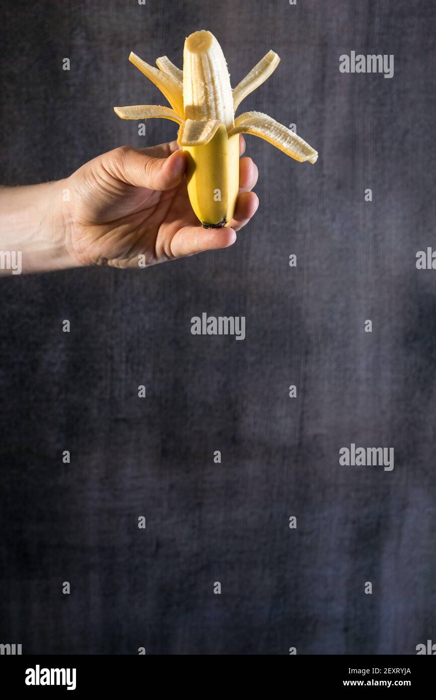 A hand holding a halfpeeled banana in the dark gray ba Stock Photo Alamy