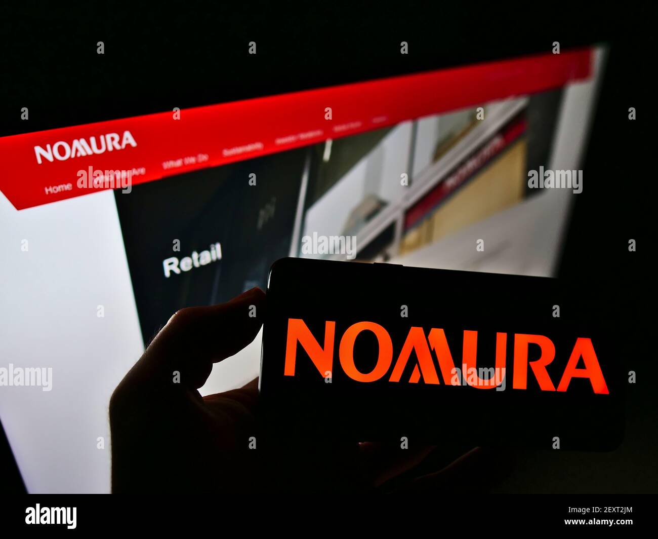 Person holding smartphone with logo of Japanese financial company Nomura Holdings KK on screen in front of business web page. Focus on phone display. Stock Photo