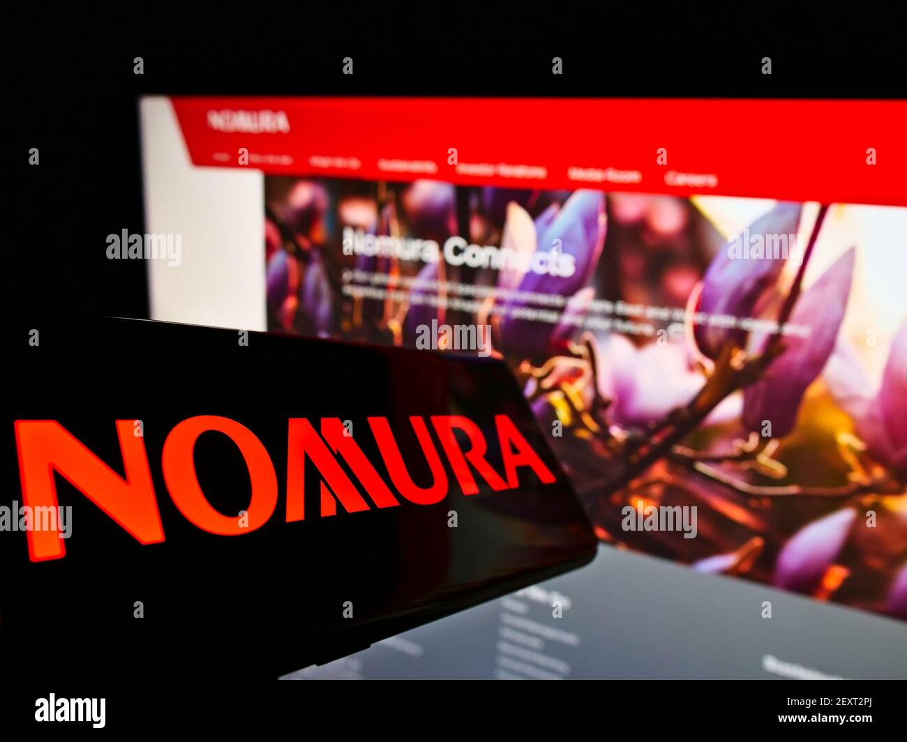 Cellphone with logo of Japanese financial company Nomura Holdings K.K. on screen in front of business website. Focus on center of phone display. Stock Photo