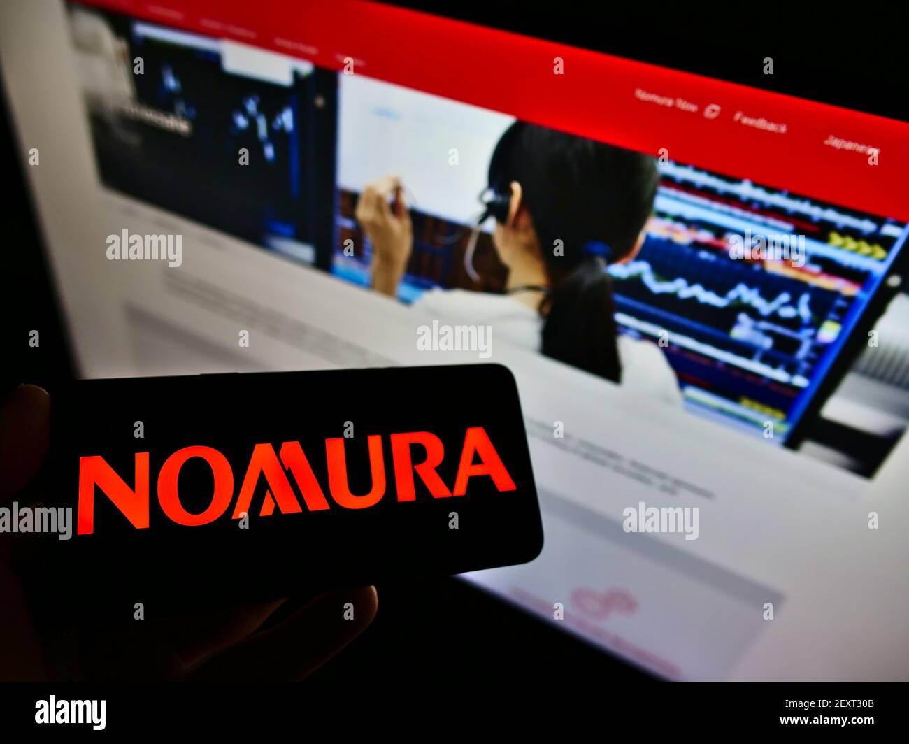 Person holding smartphone with logo of Japanese financial company Nomura Holdings K.K. on screen in front of website. Focus on phone display. Stock Photo