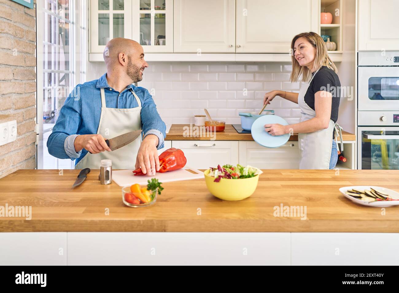 A happy young couple is enjoying and preparing a healthy meal. He cuts vegetables, she cooks spaghetti. . High quality photo Stock Photo