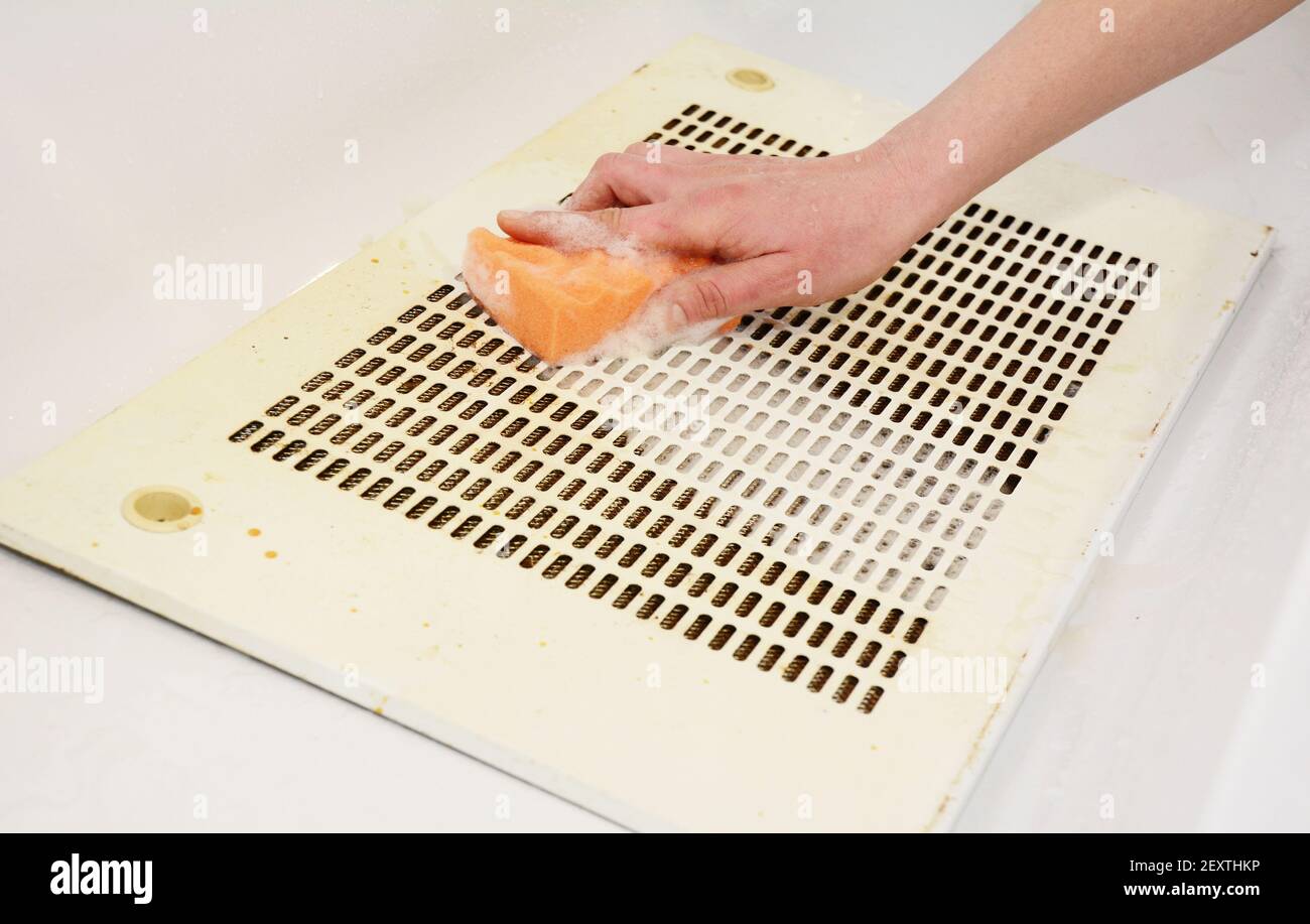 Regular kitchen exhaust hood cleaning: A woman is cleaning a greasy and dusty metal grate filter from a kitchen range hood, extraction hood, cooker ho Stock Photo