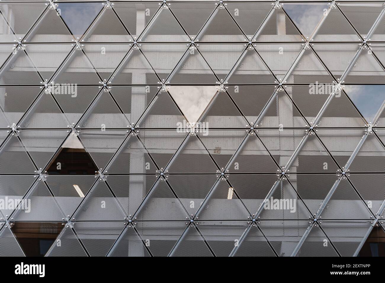 Modern building facade features a triangles pattern. Construction contemporary exterior made of grey iron triangle repetition where sky reflects into Stock Photo