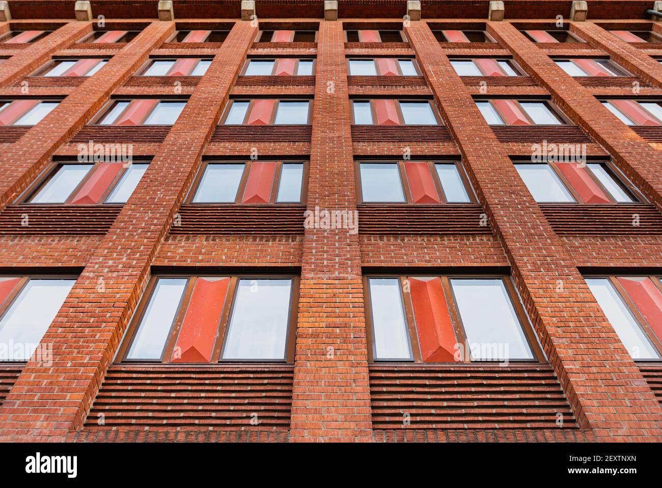 Modern residential building features a facade made of orange bricks. Windows repetition or window pattern on a orange firebrick covered exterior Stock Photo