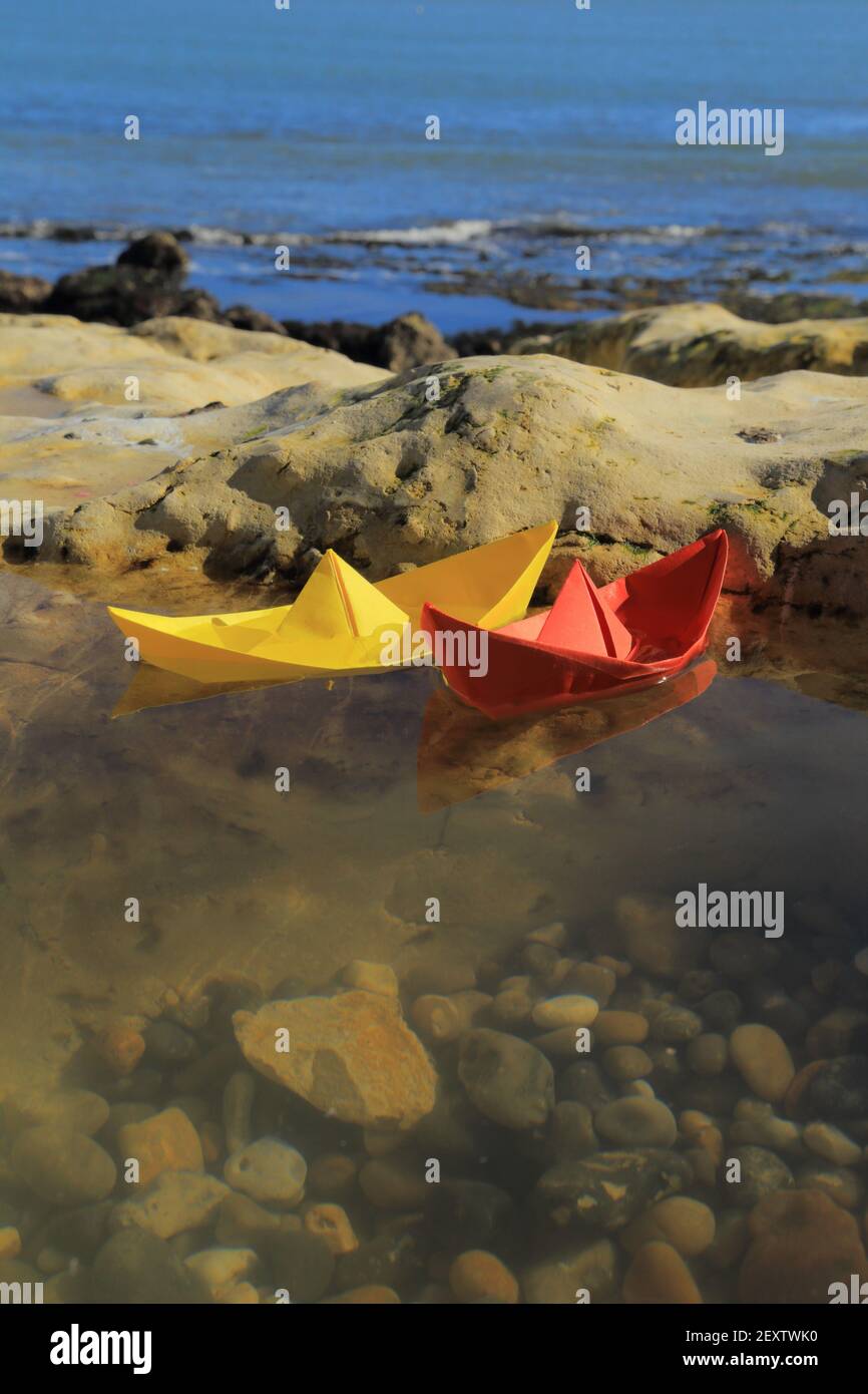 Paper boats in puddle on the rocky beach near village of Beer in Devon Stock Photo