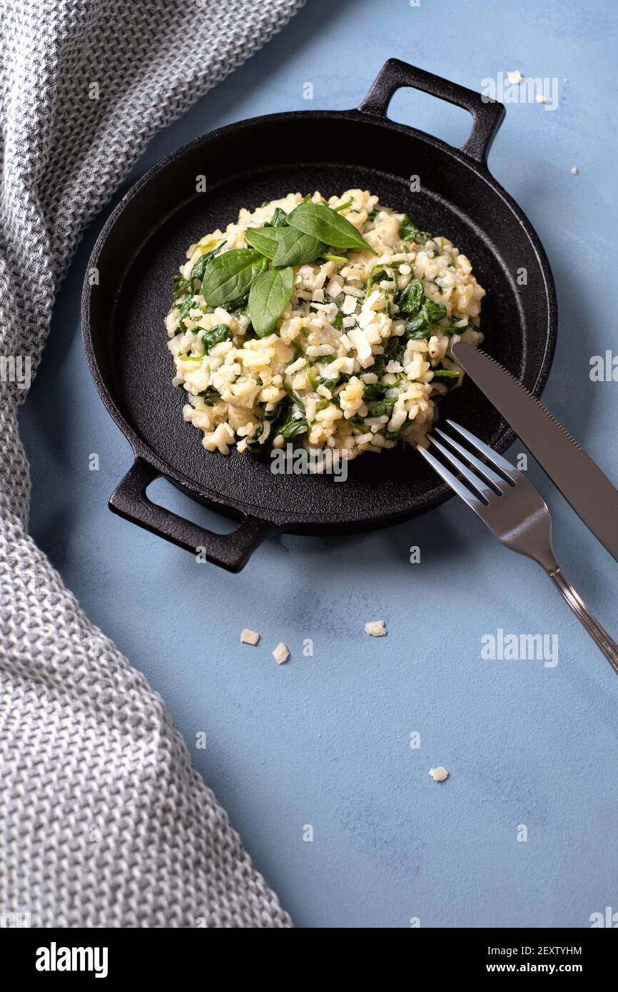 Risotto with young spinach leaves arranged in a cast iron black pan with knife and fork Stock Photo