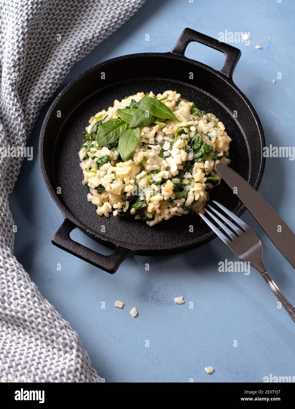 Risotto with young spinach leaves arranged in a cast iron black pan with knife and fork Stock Photo