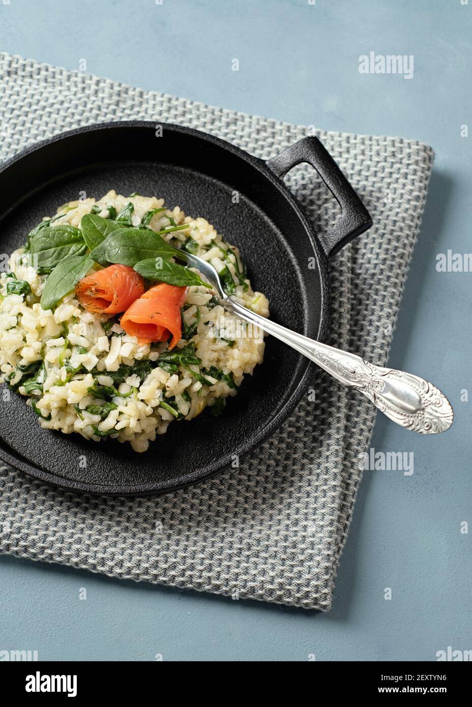 Risotto with young spinach with smoked salmon served in a cast iron black pan with knife and fork Stock Photo