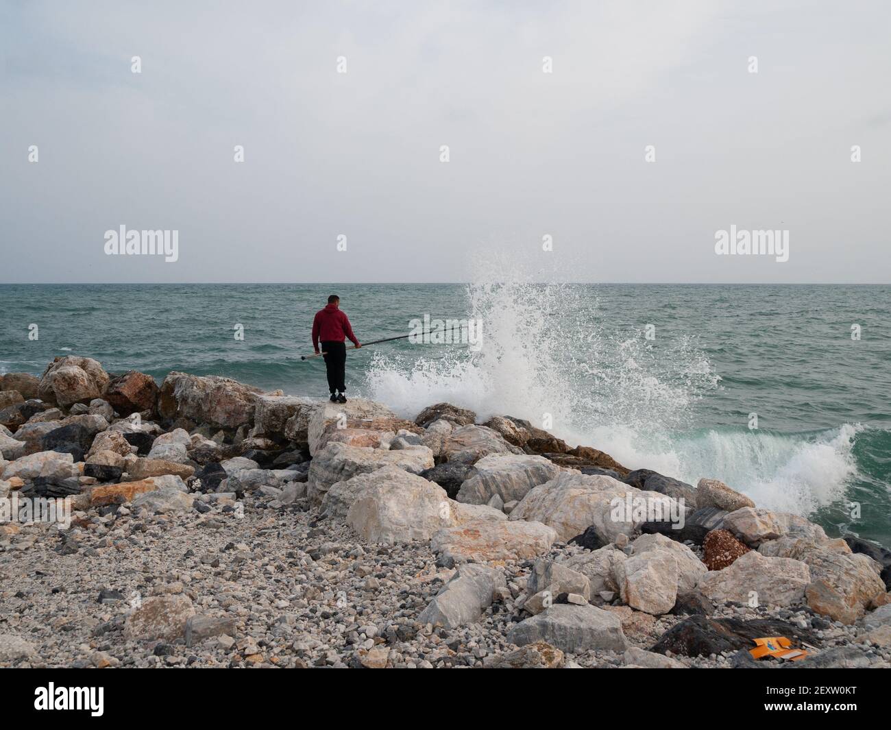 Fisherman holds his pole between both legs as waves crash into La Térmica pier under a stormy sky. (Photo by Shay Conaghan/Pacific Press) Credit: Pacific Press Media Production Corp./Alamy Live News Stock Photo