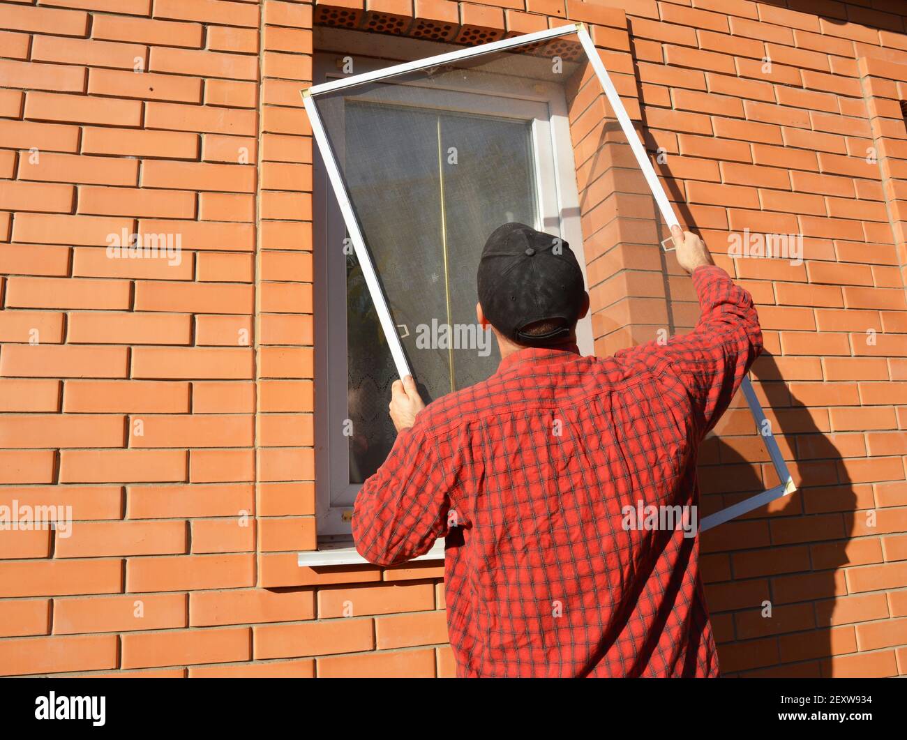 A man is installing a mosquito screen, net, panel insect screen on the window outdoors to protect his house from flies, mosquitoes, and bugs. Stock Photo