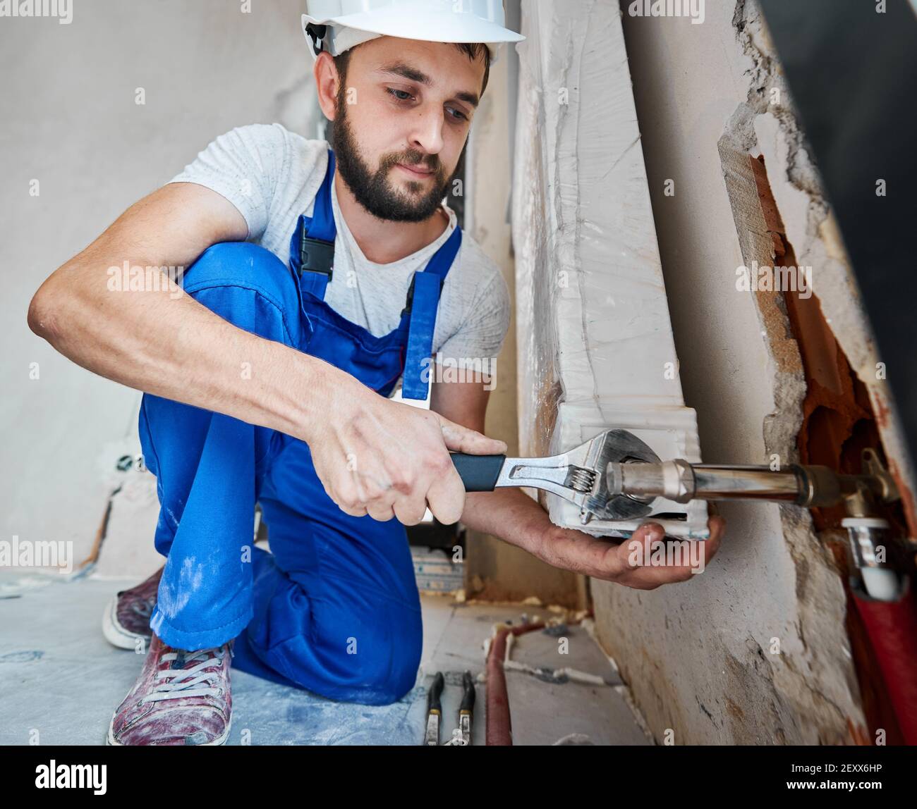 Horizontal snapshot of handsome plumber screwing plumbing fittings with a wrench. Close-up of a strong arm working with a tool during installation works in new apartment. Construction concept Stock Photo