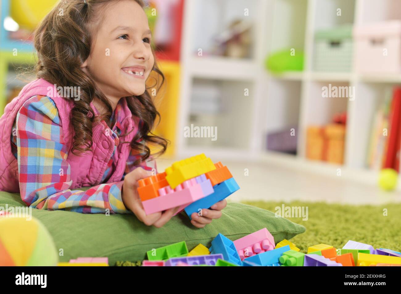 Curly little girl playing with colorful plastic blocks Stock Photo - Alamy