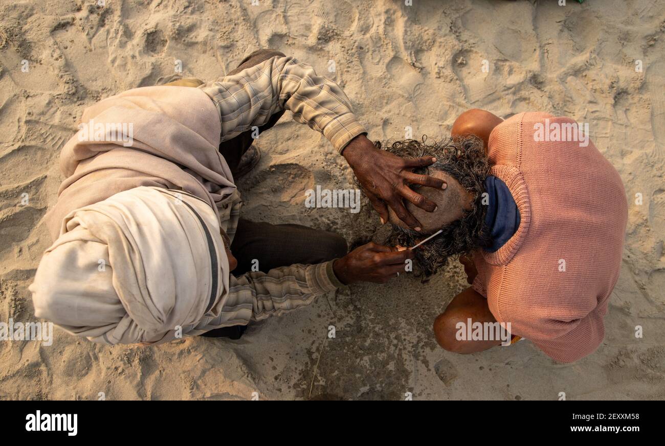 a barber cutting the hair of pilgrim during the kumbh mela in haridawar.kumbh is the largest congregation on the earth. Stock Photo