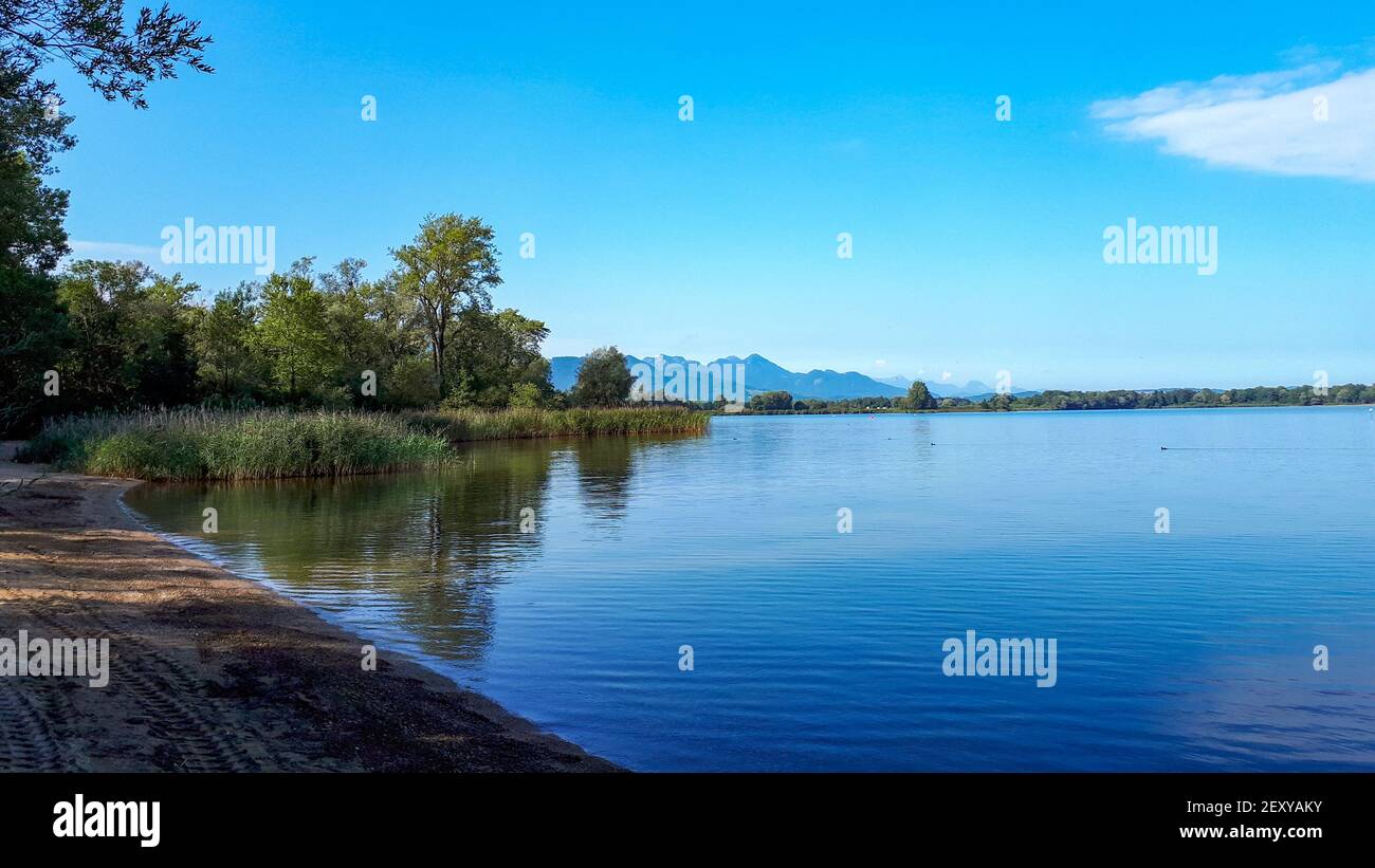 Peaceful scene at lake Chiemsee with blue clear sky and mountains in the background. Panoramic view of the beach of lake Chiemsee in summer Stock Photo