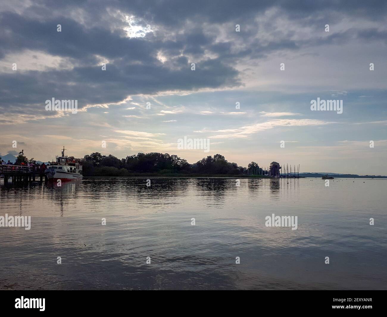 sunset over lake Chiemsee with tree silhouettes at the horizon in summer. Tranquil scene with water and cloudy evening sky Stock Photo