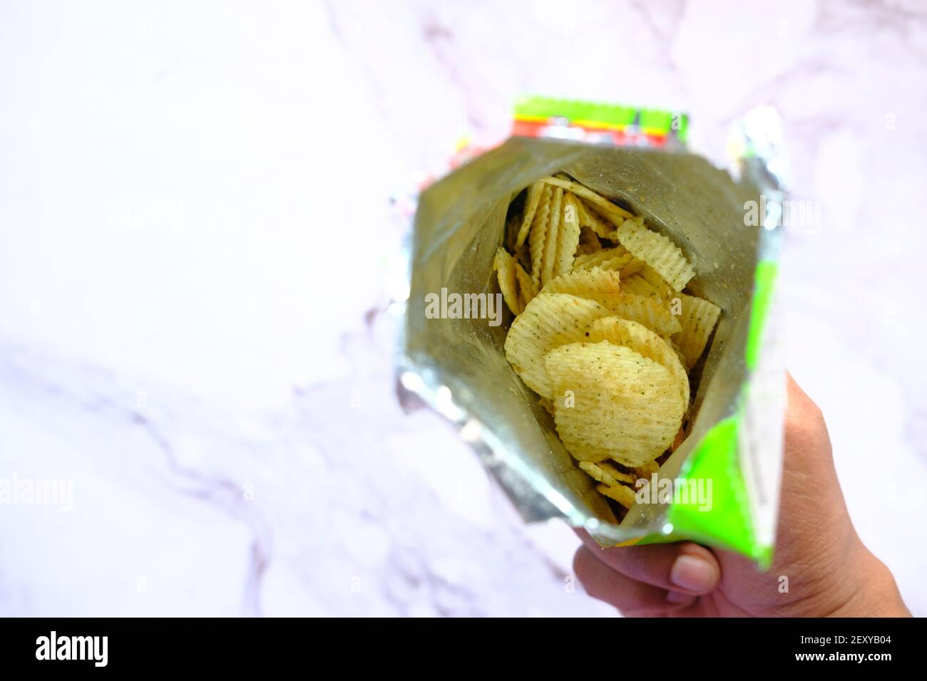 holding a packer of tasty potato chips on wooden background . Stock Photo
