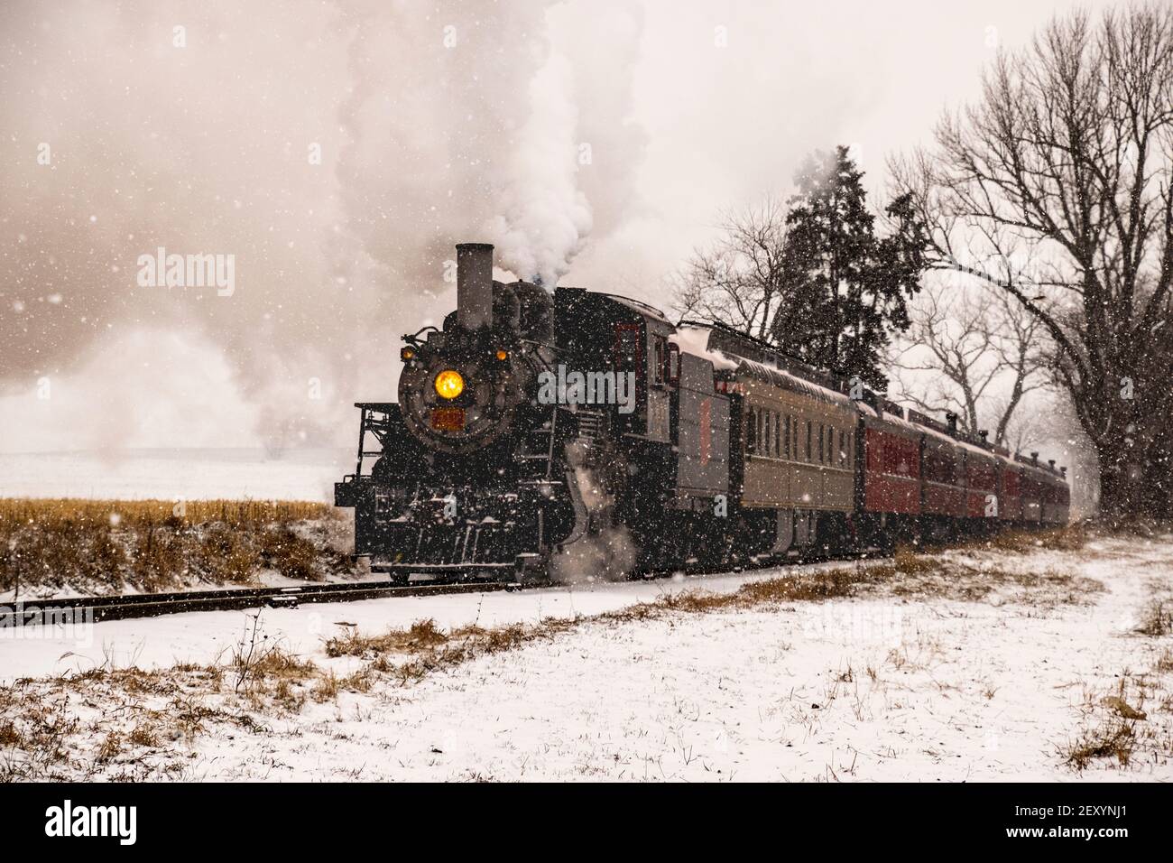 View of An Antique Restored Steam Locomotive Blowing Smoke and Steam Traveling Thru Farmlands and Countryside in a Snow Storm Stock Photo