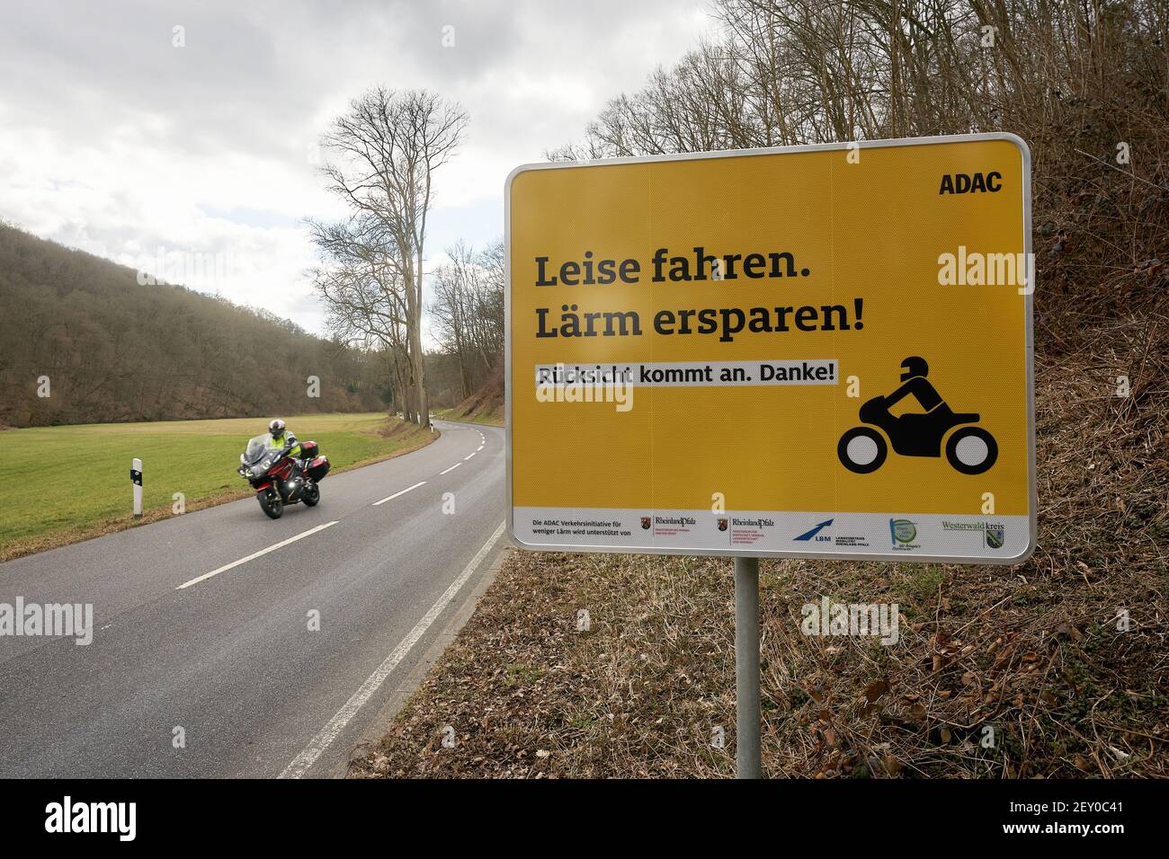 Montabaur, Germany. 05th Mar, 2021. A motorcyclist rides past a sign on the country road in the Gelbach valley asking bikers to ride quietly and considerately. Before the start of the season, the ADAC, supported by the state of Rhineland-Palatinate, is launching a pilot project against motorcycle noise. (to dpa "Pilot project and further measures against motorcycle noise at the start of the season") Credit: Thomas Frey/dpa/Alamy Live News Stock Photo